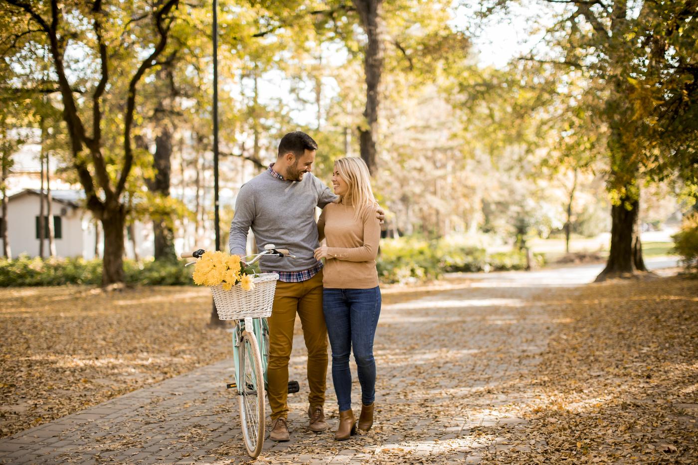 A young couple walking a bicycle through an autumn morning